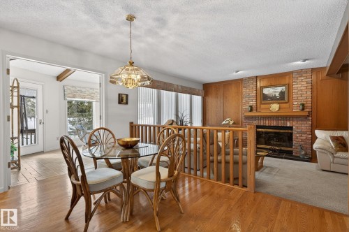 Dining area featuring wood-finish flooring, a glass-top table, and a tiered chandelier - 848 Wheeler Road W, Edmonton, AB - Indoor Photo Showing Dining Room With Fireplace