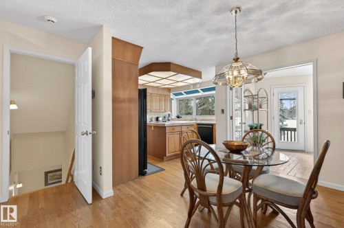 Dining area with wood-finish flooring, featuring a glass-top table and a decorative chandelier - 848 Wheeler Road W, Edmonton, AB - Indoor Photo Showing Dining Room