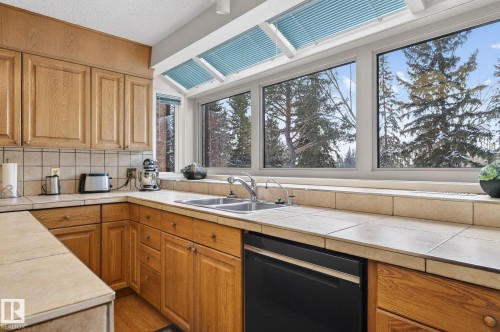 Kitchen featuring natural wood cabinetry, ceramic tile countertops and backsplash, a stainless steel double sink, and a black built-in dishwasher - 848 Wheeler Road W, Edmonton, AB - Indoor Photo Showing Kitchen With Double Sink