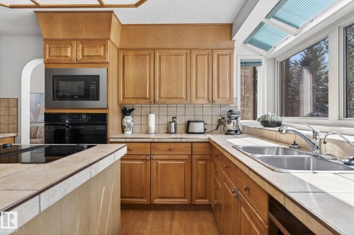 Kitchen featuring wood cabinetry, tile countertops, and wood-finish flooring - 848 Wheeler Road W, Edmonton, AB - Indoor Photo Showing Kitchen With Double Sink
