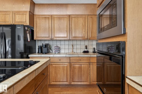 Kitchen featuring wood-finish cabinetry, tile countertops, and a white square tile backsplash - 848 Wheeler Road W, Edmonton, AB - Indoor Photo Showing Kitchen