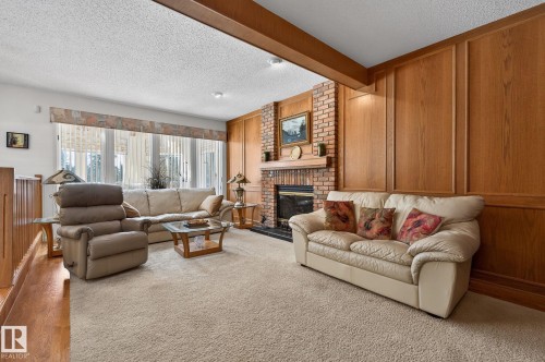 Spacious living area featuring a brick-faced fireplace with a mantel, extensive wood paneling, and a large window wall - 848 Wheeler Road W, Edmonton, AB - Indoor Photo Showing Living Room With Fireplace