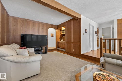 Wood-paneled living area featuring a built-in wet bar with integrated lighting, an arched entryway, and neutral carpet flooring - 848 Wheeler Road W, Edmonton, AB - Indoor Photo Showing Living Room