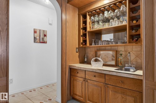 Built-in wet bar featuring a stainless steel sink, tile countertop, and wood cabinetry - 848 Wheeler Road W, Edmonton, AB - Indoor Photo Showing Other Room