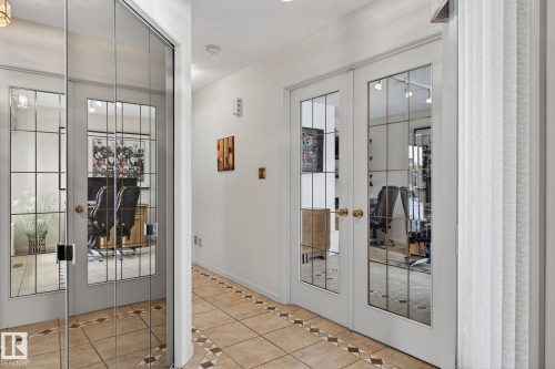 Hallway featuring tile flooring with decorative inlay, white walls, and two sets of double French doors with grid-patterned glass panels - 848 Wheeler Road W, Edmonton, AB - Indoor Photo Showing Other Room