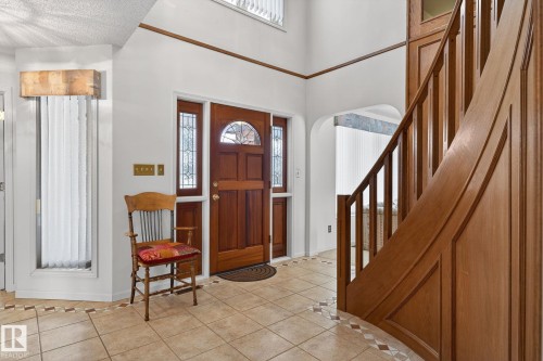 Two-story foyer featuring a prominent wood staircase, tile flooring with decorative inlay, a wood-paneled entry door with leaded glass, and tall windows with vertical blinds - 848 Wheeler Road W, Edmonton, AB - Indoor Photo Showing Other Room