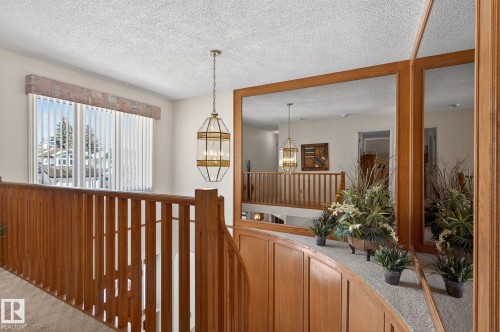Hardwood railing and banister with a wood-paneled wall, overhead chandelier, and vertical blinds on a large window - 848 Wheeler Road W, Edmonton, AB - Indoor Photo Showing Other Room