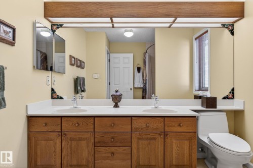 Bathroom vanity featuring dual under-mount sinks, a white countertop, and wood-finish cabinetry with multiple storage drawers and doors - 848 Wheeler Road W, Edmonton, AB - Indoor Photo Showing Bathroom