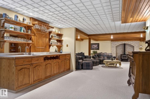 Lower level entertainment space featuring a wet bar with integrated shelving, a wood-finish cabinet base, and a tiled drop ceiling - 848 Wheeler Road W, Edmonton, AB - 