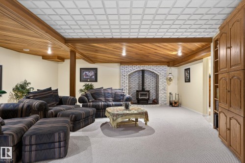 Spacious living area featuring a wood-burning stove within an arched white brick surround, wood-paneled ceiling accents, and a complementary wood built-in shelving unit - 848 Wheeler Road W, Edmonton, AB - Indoor
