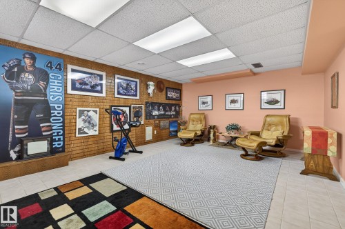 Spacious room featuring a drop-tile ceiling with integrated lighting, a textured brick accent wall, light-toned wall paint, and tile flooring - 848 Wheeler Road W, Edmonton, AB - Indoor