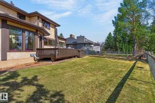 Expansive backyard featuring a manicured lawn, a wooden deck, mature trees, and chain-link fencing - 848 Wheeler Road W, Edmonton, AB - Outdoor