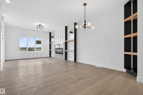 Spacious living area featuring wood-finish flooring, a contemporary fireplace with a textured surround, and a ceiling-mounted light fixture - 45 River Birch, St. Albert, AB - Indoor