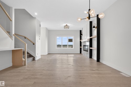 Spacious living area featuring light wood-finish flooring and a contemporary fireplace with a sleek surround and integrated shelving - 45 River Birch, St. Albert, AB - Indoor Photo Showing Other Room