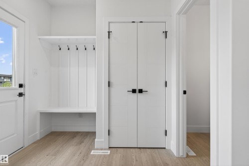 Entryway featuring wood-finish flooring, a white built-in bench with shiplap backing, black coat hooks, and white paneled bi-fold doors with matte black hardware - 45 River Birch, St. Albert, AB - Indoor Photo Showing Other Room