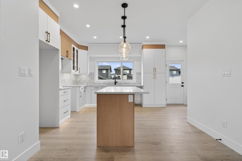 Contemporary kitchen featuring a central island with a light wood-finish base, a light-toned countertop, and an overhead multi-bulb pendant light fixture - 45 River Birch, St. Albert, AB - Indoor Photo Showing Kitchen With Upgraded Kitchen