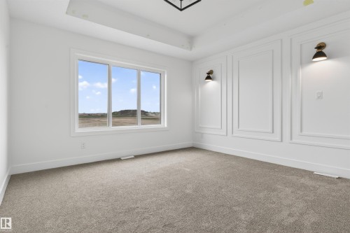 Expansive room with large triple-pane window, tray ceiling, decorative wall molding, and two wall-mounted sconces - 45 River Birch, St. Albert, AB - Indoor Photo Showing Other Room