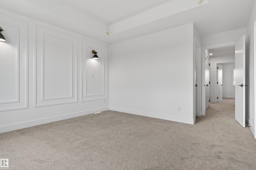 Spacious room featuring carpeted flooring, white baseboards, and a paneled accent wall with integrated sconce lighting - 45 River Birch, St. Albert, AB - Indoor Photo Showing Other Room