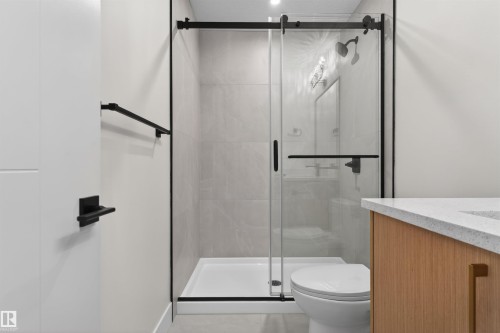 Modern bathroom featuring a glass-enclosed shower with matte black hardware, light-toned wall tiling, a white shower pan, and a toilet - 45 River Birch, St. Albert, AB - Indoor Photo Showing Bathroom