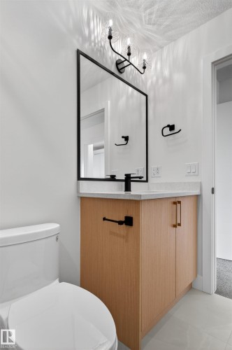 Modern bathroom featuring a wood-finish vanity with a light-colored countertop, a rectangular black-framed mirror, and a three-light sconce with textured glass shades - 45 River Birch, St. Albert, AB - Indoor Photo Showing Bathroom