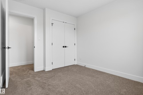 Carpeted room featuring a white interior door with black hardware, a built-in closet with double white doors and black hardware, and crisp white baseboards - 45 River Birch, St. Albert, AB - Indoor Photo Showing Other Room