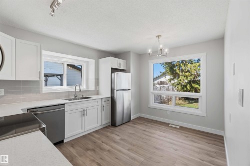 Bright kitchen featuring white cabinetry, stainless steel appliances, light gray subway tile backsplash, and wood-finish flooring - 119 Dorchester Drive, St. Albert, AB - Indoor Photo Showing Kitchen