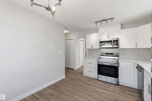 Modern kitchen featuring white cabinetry, stainless steel appliances, light-toned countertops, a subway tile backsplash, and wood-finish flooring - 119 Dorchester Drive, St. Albert, AB - Indoor Photo Showing Kitchen