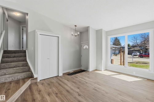 Bright living space featuring wood-finish flooring, a contemporary chandelier, large picture windows, a front entry door with a decorative glass insert, and a stairway with carpeted treads - 119 Dorchester Drive, St. Albert, AB - Indoor Photo Showing Other Room