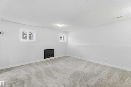 Spacious room featuring light gray carpeting, neutral wall finishes, and two egress windows with white trim - 119 Dorchester Drive, St. Albert, AB - Indoor Photo Showing Other Room