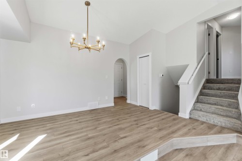 Open concept living space featuring wood-finish flooring, a contemporary six-light chandelier, arched entryway, and staircase with carpeted treads and white railing - 119 Dorchester Drive, St. Albert, AB - Indoor Photo Showing Other Room