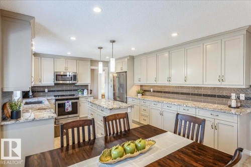 The kitchen features extensive cabinetry, light-colored granite countertops, and stainless steel appliances - 954 Rice Road, Edmonton, AB - Indoor Photo Showing Kitchen With Stainless Steel Kitchen With Upgraded Kitchen
