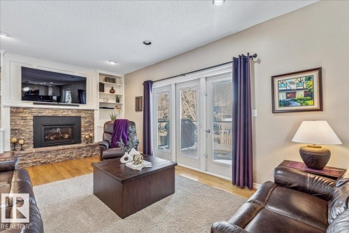 Living room featuring hardwood floors, a stacked stone fireplace with a mantel, built-in shelving, and a pair of glass French doors - 954 Rice Road, Edmonton, AB - Indoor Photo Showing Living Room With Fireplace