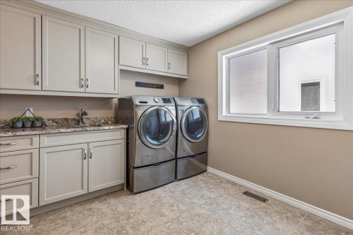 This laundry room features light-colored cabinetry with silver hardware, a granite countertop with a sink, and a large window providing natural light - 954 Rice Road, Edmonton, AB - Indoor Photo Showing Laundry Room