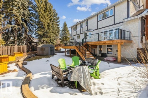The property features a spacious rear yard with a wooden deck, glass railings, and stairs leading to a patio area - 954 Rice Road, Edmonton, AB - Outdoor With Deck Patio Veranda