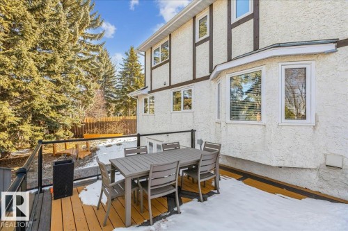 The property features an exterior with light-colored stucco and dark trim details, bay windows, and a wood deck with glass panel railings - 954 Rice Road, Edmonton, AB - Outdoor With Deck Patio Veranda With Exterior