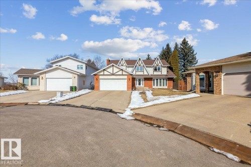 The property features a brick and white exterior with dark brown trim, a prominent white garage door, and a paved driveway - 954 Rice Road, Edmonton, AB - Outdoor With Facade