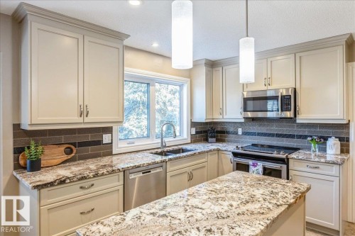 The kitchen features light-colored cabinetry with crown molding, granite countertops, a subway tile backsplash, and stainless steel appliances including a microwave, oven, and dishwasher - 954 Rice Road, Edmonton, AB - Indoor Photo Showing Kitchen With Stainless Steel Kitchen With Upgraded Kitchen