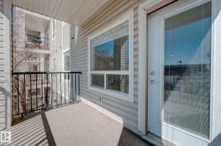 Private balcony featuring light-colored siding, a black metal railing, and a window and door with integrated blinds - 
