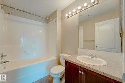 Bathroom featuring a white tub and shower combination, a dark wood-finish vanity with a light countertop, a single basin sink with chrome fixtures, a large wall-mounted mirror, and tile flooring - 