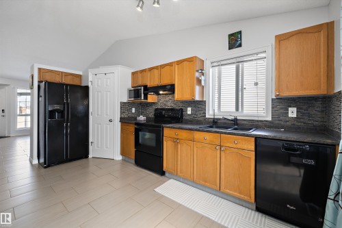 Kitchen featuring light wood cabinetry, dark countertops, and a mosaic tile backsplash - 1811 37 Avenue, Edmonton, AB - Indoor Photo Showing Kitchen With Double Sink