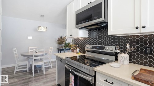 Kitchen featuring white upper and lower cabinetry with black hardware, stainless steel appliances, and a black hexagonal tile backsplash - 13533 119 Street, Edmonton, AB - Indoor Photo Showing Kitchen