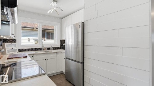 Kitchen featuring white cabinetry, light countertops, stainless steel appliances, a black hexagonal tile backsplash, and a white plank accent wall - 13533 119 Street, Edmonton, AB - Indoor Photo Showing Kitchen With Stainless Steel Kitchen