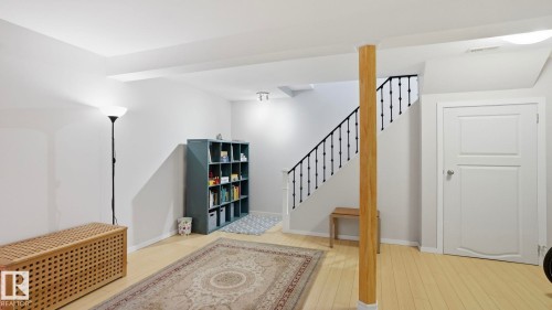 Finished lower-level space featuring light wood-finish flooring and a staircase with black metal balusters - 13533 119 Street, Edmonton, AB - Indoor Photo Showing Other Room