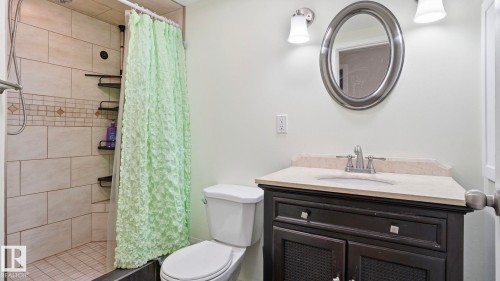 Bathroom featuring a tiled shower with decorative accent border, a dark wood vanity with a light-colored countertop, and an oval mirror with brushed nickel hardware - 13533 119 Street, Edmonton, AB - Indoor Photo Showing Bathroom