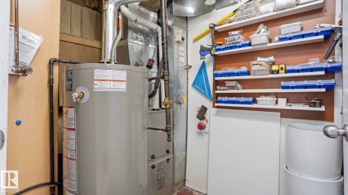 Dedicated utility space featuring a water heater and furnace with exposed ductwork, alongside a built-in wall-mounted shelving unit for organized storage - 13533 119 Street, Edmonton, AB - Indoor Photo Showing Basement