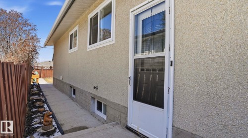 Exterior featuring stucco siding with a stone-finish foundation, multiple white-framed windows, a white storm door, and a concrete pathway - 13533 119 Street, Edmonton, AB - Outdoor With Exterior