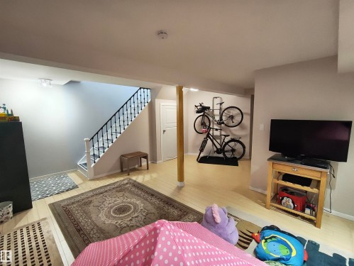 Open-concept lower level featuring light wood-finish flooring, a staircase with black metal balusters and white risers, a light gray wall finish, a recessed ceiling light fixture, and a white interior door - 13533 119 Street, Edmonton, AB - Indoor Photo Showing Other Room