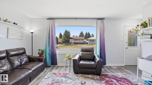 Living area featuring wood-finish flooring, a large picture window, and a white paneled entry door with decorative glass - 13533 119 Street, Edmonton, AB - Indoor Photo Showing Living Room