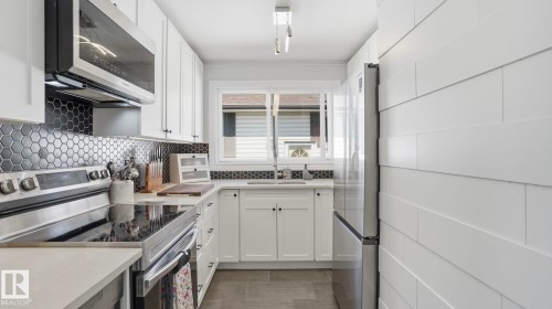 Modern kitchen featuring white shaker cabinetry, stainless steel appliances, and a black hexagonal tile backsplash - 13533 119 Street, Edmonton, AB - Indoor Photo Showing Kitchen With Upgraded Kitchen