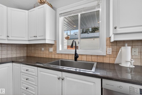 The kitchen features white cabinetry, a tiled backsplash, dark countertops, and a stainless steel sink with a modern faucet - 2 Sturgeon Road, St. Albert, AB - Indoor Photo Showing Kitchen